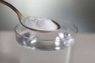 Açık gri arka planda, su bardağının üzerinde kabartma tozu bulunan kaşık, yakın plan.