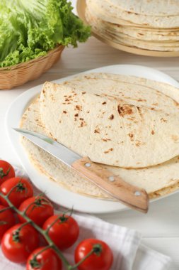 Lezzetli ev yapımı tortilla, domates, marul ve bıçak beyaz ahşap masada.