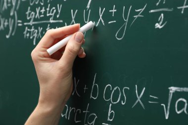 Teacher writing down math equation on green board, closeup