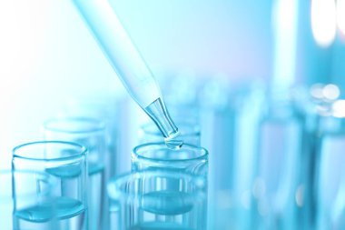 Açık mavi arkaplanda pipetten test tüpüne sıvı damlatılıyor, yakın plan.
