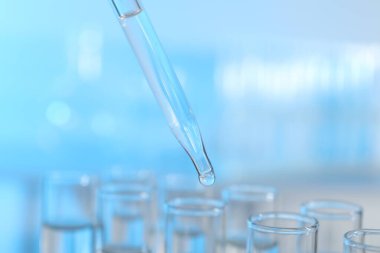 Işık arka planında pipetten test tüpüne sıvı damlatılıyor, yakın plan