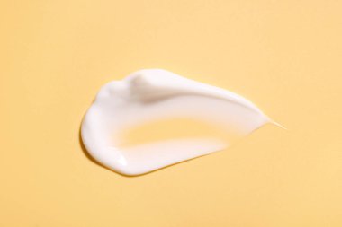 Soluk sarı arka planda yüz kremi örneği, üst görünümde.