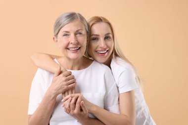 Family portrait of young woman and her mother on beige background