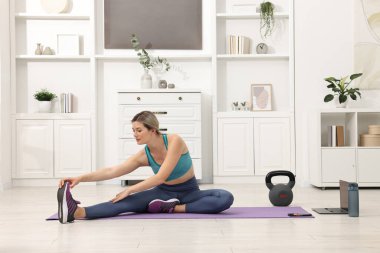 Online fitness trainer. Woman doing exercise near laptop at home