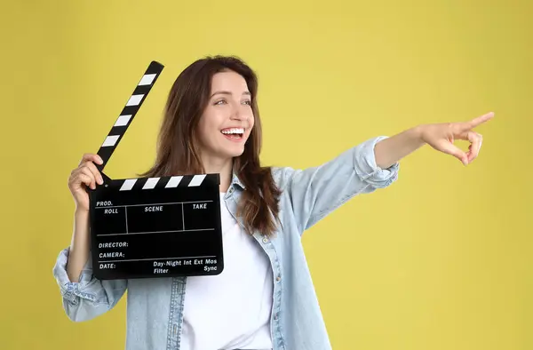 stock image Making movie. Smiling woman with clapperboard pointing at something on yellow background