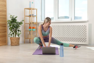 Online fitness trainer. Woman doing exercise near laptop at home