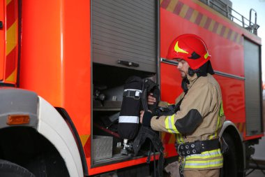 Üniformalı itfaiyeci ve güvenlik ekipmanları istasyonda itfaiye aracının yanında.