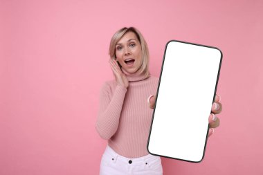 Pembe arka planda boş ekranlı cep telefonu gösteren bir kadın. Tasarım için model