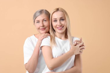 Family portrait of young woman and her mother on beige background