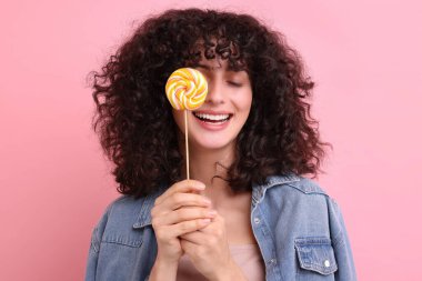 Güzel bir kadın pembe arka planda lolipopla gözlerini kapatıyor.