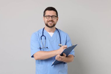 Açık gri arka planda panosu olan gülümseyen doktor.