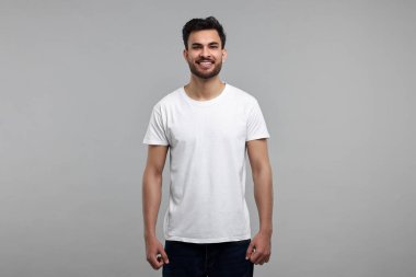 Gri arkaplanda beyaz tişörtlü gülen adam.