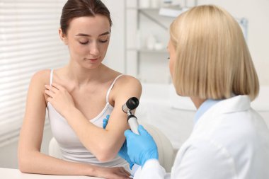 Dermatoskoplu bir dermatolog klinikteki hastayı muayene ediyor.