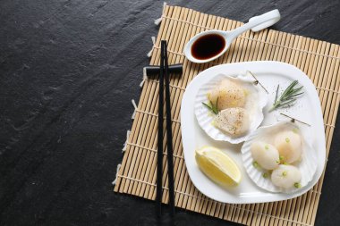 Yeşil soğanlı çiğ deniz tarağı, biberiye, limon ve soya sosu koyu dokulu masa, üst manzara. Metin için boşluk