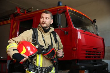 Kasklı ve maskeli itfaiyeci kırmızı itfaiye aracının yanında.