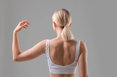 Gri arka planda spor vücudunu gösteren bir kadın.