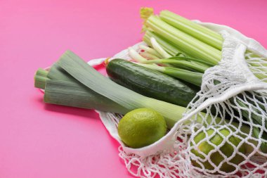 Parlak pembe arka planda farklı sebzeler içeren ip torbası, yakın plan.