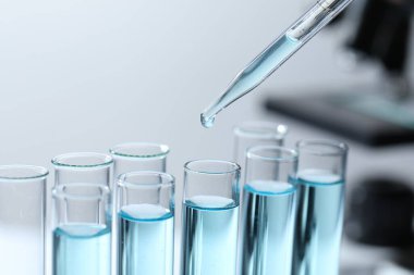 Bulanık arkaplanda pipetten test tüpüne sıvı damlatılıyor.
