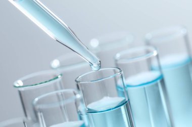 Işık arka planında pipetten test tüpüne sıvı damlatılıyor, yakın plan