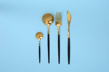 Açık mavi arka planda altın çatal bıçak seti düz yatıyordu.