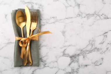 Beyaz mermer masa üzerinde şık çatal bıçak seti ve peçete, üst manzara. Metin için boşluk