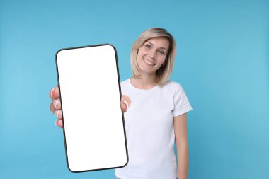 Açık mavi arka planda boş ekranlı cep telefonu gösteren mutlu bir kadın. Tasarım için model