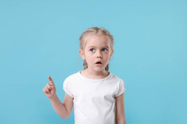 Açık mavi arka plandaki bir şeyi işaret eden sevimli küçük kız, mesaj için yer.