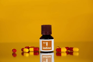 Bir şişe tıbbi iyot ve turuncu arka planda haplar.