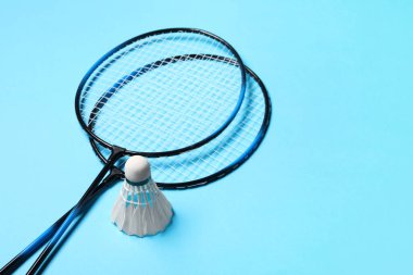 Tüy badminton mekik horozları ve raketler açık mavi arkaplan, metin için boşluk