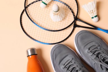 Tüy badminton mekikleri, spor ayakkabıları ve bej arka planda şişe, düz uzanma