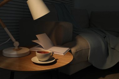 Şık bir lamba, kitap ve çay yan masada, kanepede.