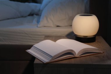 Gece lambası ve kitap yatağın yanındaki komodinin üzerinde.