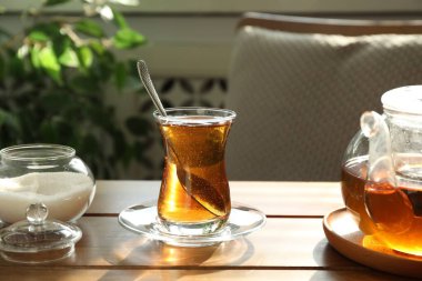 Bardakta Aromatik çay, içeride ahşap masada çaydanlık ve şeker