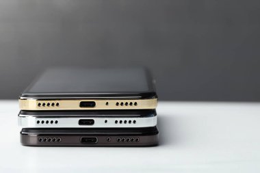 Stack of modern smartphones on white table, closeup. Space for text
