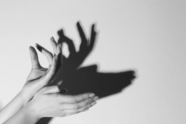 Gölge kuklası. Kadın, hafif arka planda geyik gibi el hareketi yapıyor, mesaj için yere yakın çekim yapıyor. Siyah ve beyaz etkisi