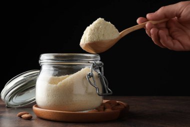 Ahşap masadaki kavanoza taze badem unu ekleyen kadın, yakın plan.