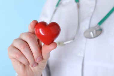Açık mavi arka planda kırmızı kalpli doktor, yakın plan.