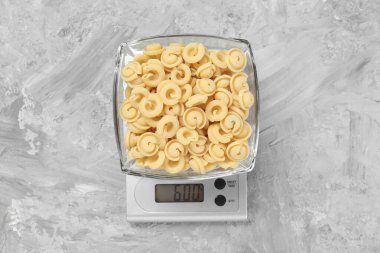 Mutfak terazisi, gri desenli masada bir kase makarna, üst manzara.