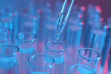 Renk arka planında pipetten test tüpüne sıvı damlatılıyor, yakın plan