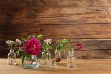 Different flowers in glass bottles on wooden table clipart