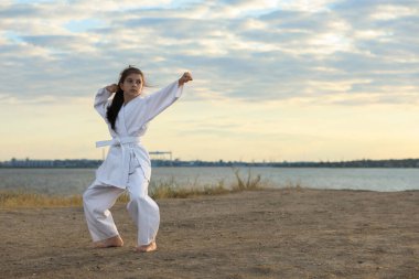 Kimonolu tatlı küçük kız nehir kenarında karate yapıyor.