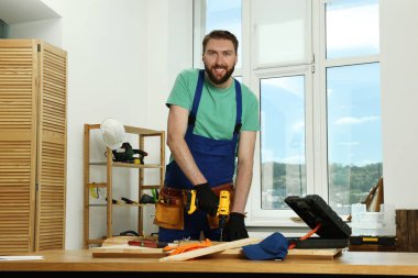 Atölyede elinde matkapla gülümseyen bir zanaatkarın portresi.