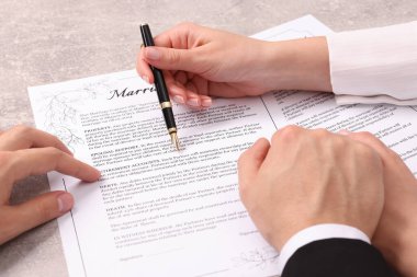 Erkek ve kadın açık gri masada evlilik sözleşmesi imzalıyor, yakın plan.