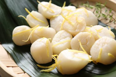 Yeşil yaprakların üzerinde kekik ve limon aromalı çiğ deniz tarakları, yakın plan.