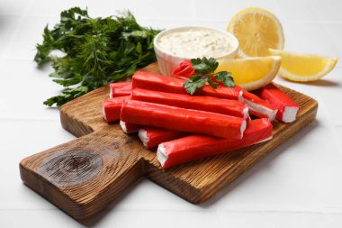 Lezzetli yengeç çubukları, sos, maydanoz ve limon parçaları beyaz masada, yakın plan.