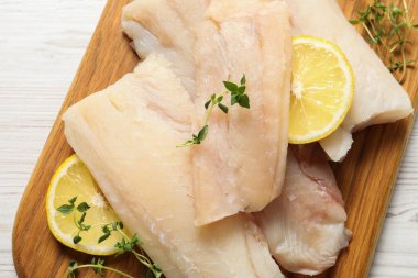 Çiğ morina balığı parçaları, beyaz ahşap masada limon ve baharatlar.