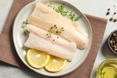 Çiğ morina balığı, baharat, mikro yeşillik ve limon tabağı gri masada, düz yerde.