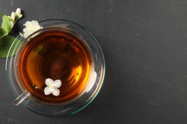 Cam bardakta Aromatik yasemin çayı, gri masada çiçekler ve yeşil yapraklar, üst manzara. Metin için boşluk
