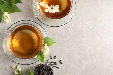 Aromatik yasemin çayı fincanlarda, çiçekler ve açık gri masada kuru yapraklar, düz yerde. Metin için boşluk