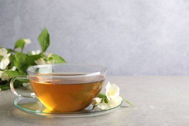 Aromatik yasemin çayı fincanda, çiçekler ve yeşil yapraklar açık gri masada, metin için boşluk